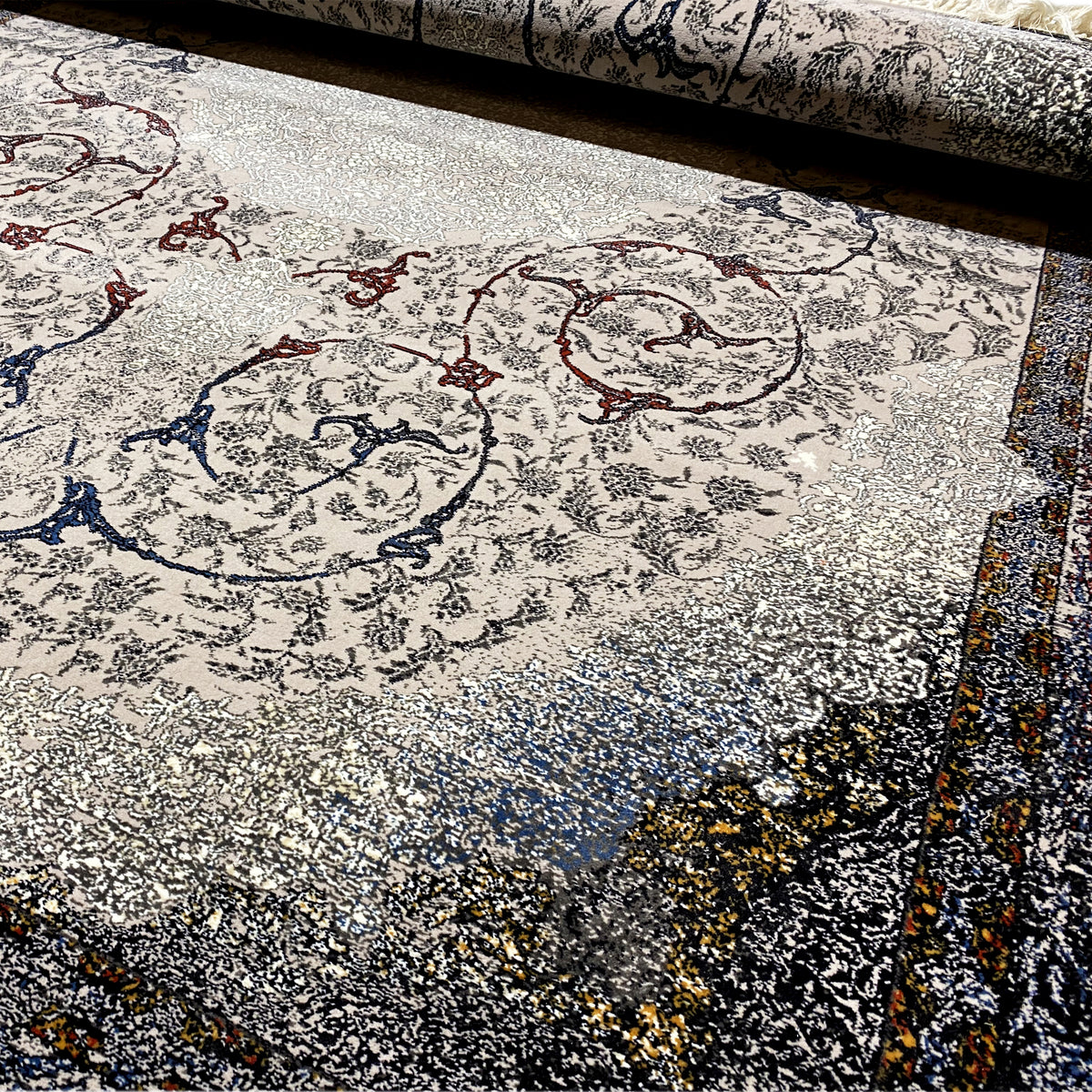 Détail de tapis orné de motifs baroques gris, bleus et rouges, avec un velours structuré et chiné
