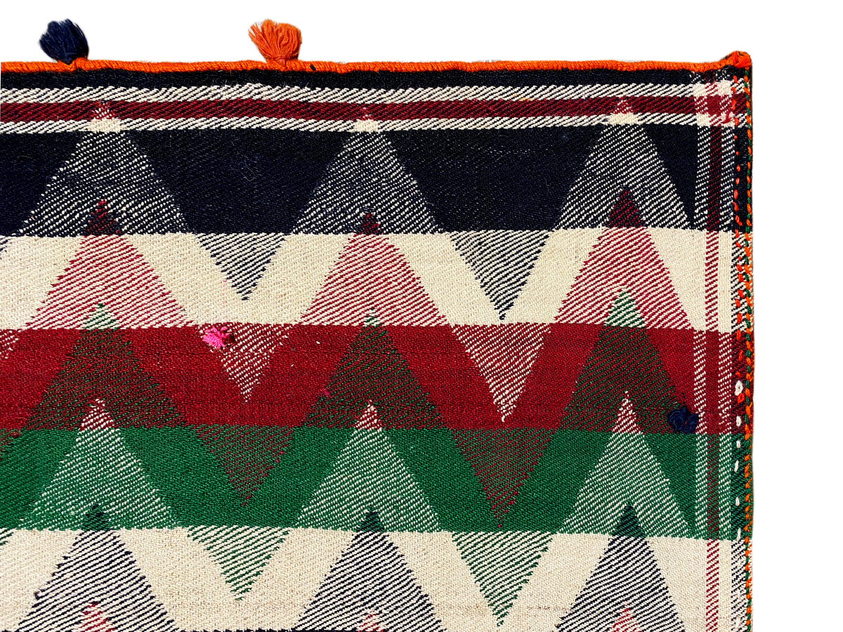 Gros plan d’un tapis jajim : motifs triangulaires et rayés aux couleurs vives, avec des pompons orange