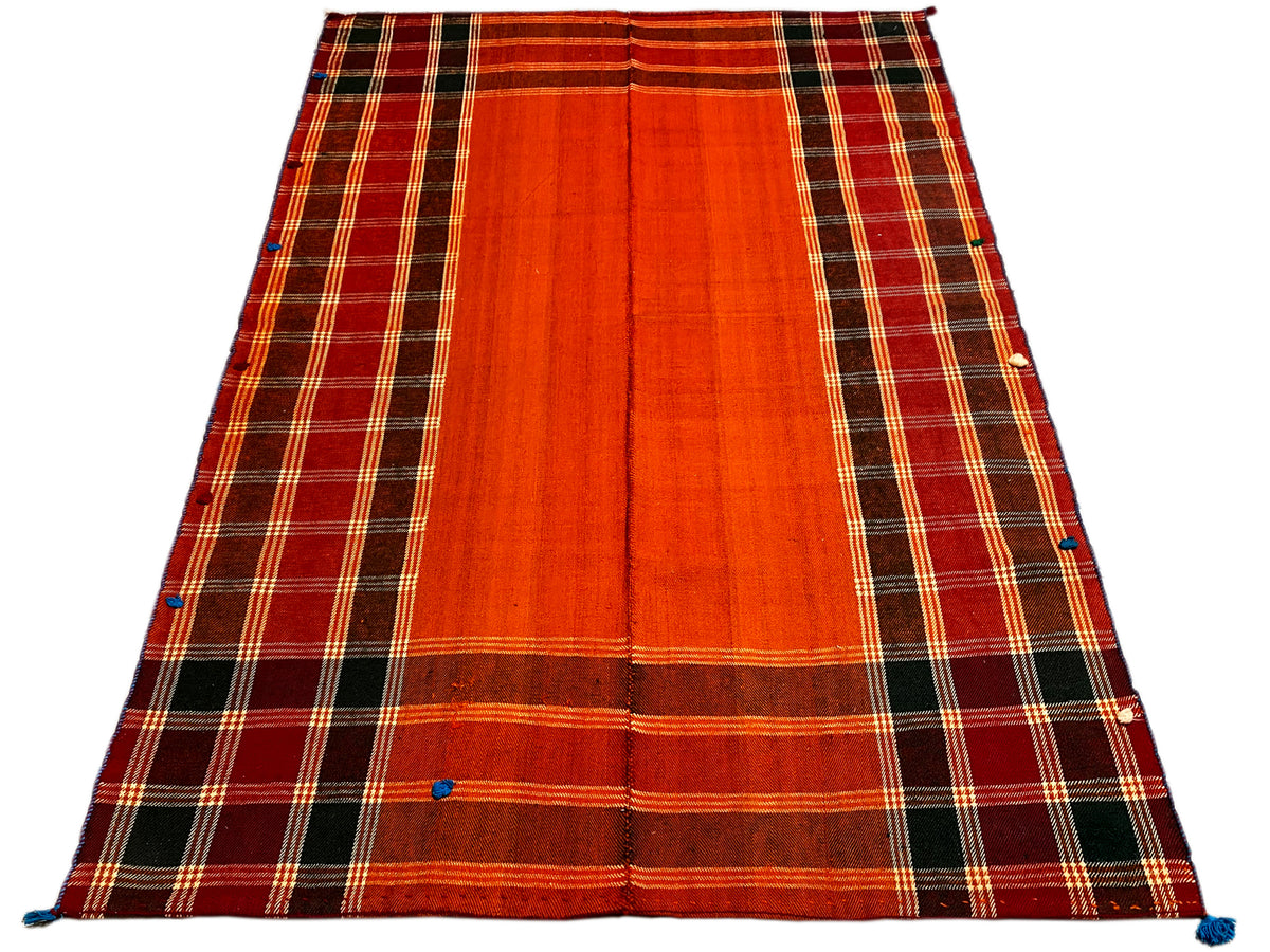 Tapis Jajim, posé en biais : surface rouge-orange avec bord à carreaux foncé et attaches bleues