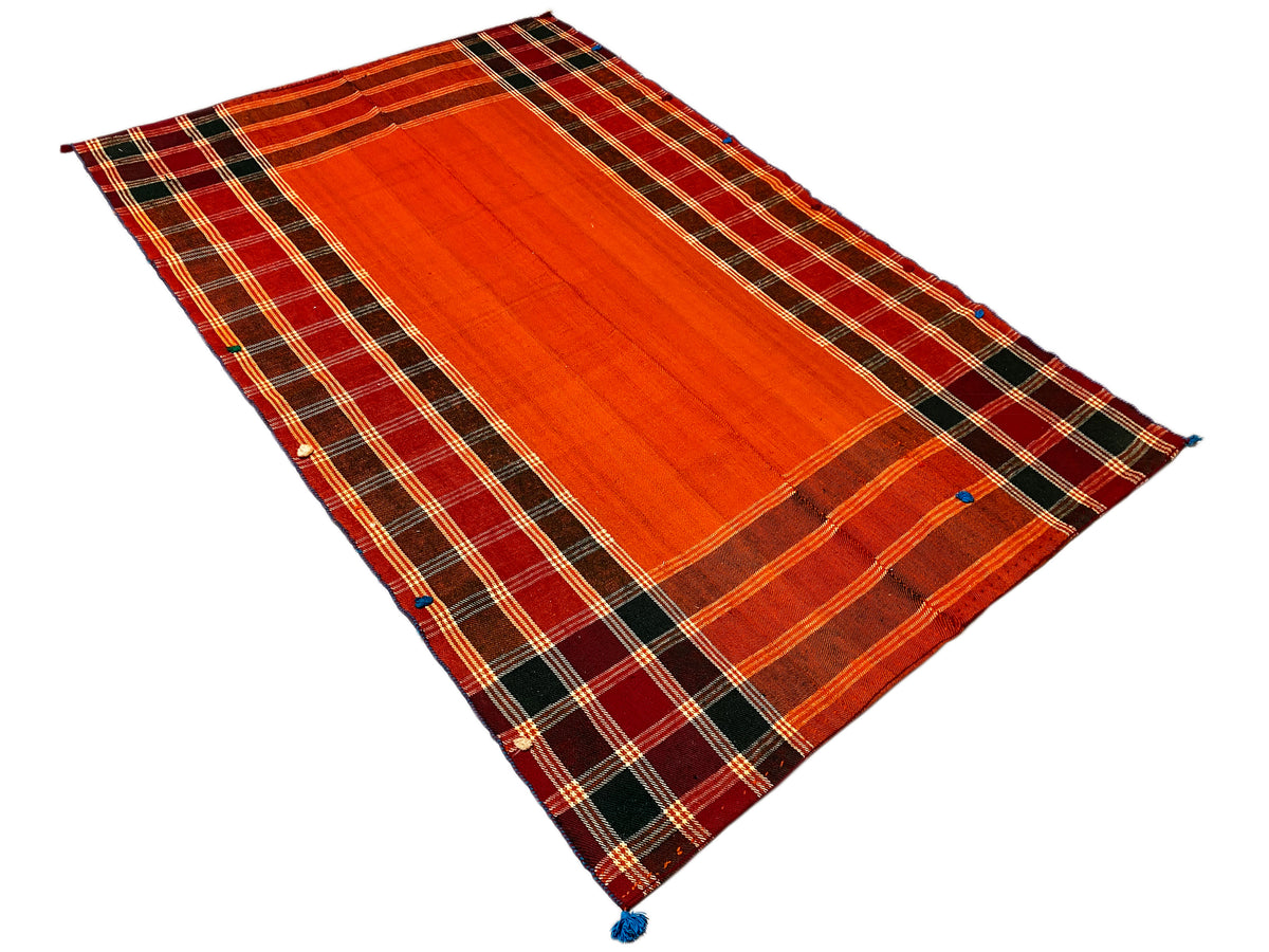 Vue en perspective d’un tapis Jajim : bande centrale rouge-orange, bordure à carreaux foncés