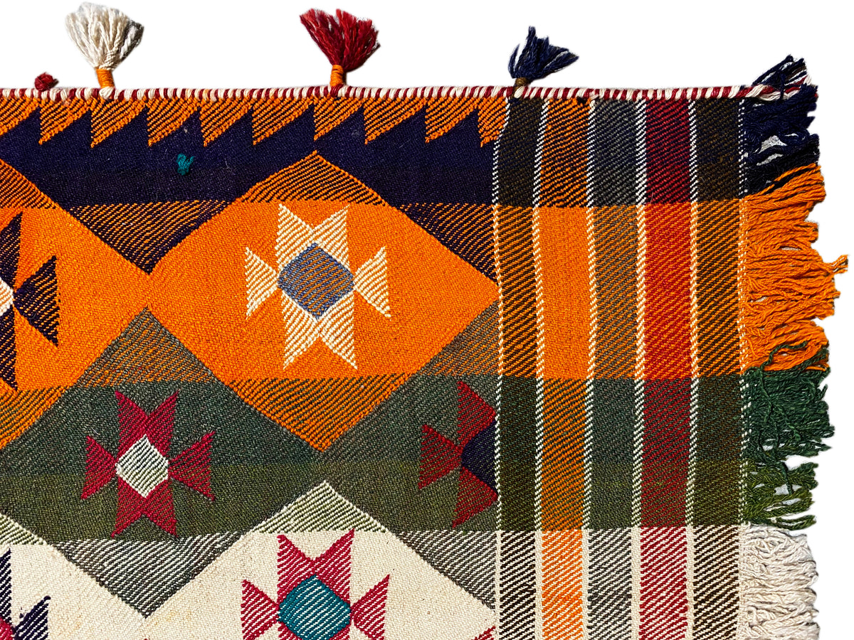 Gros plan d’un tapis Jajim : motifs orange à carreaux et losanges, franges et glands