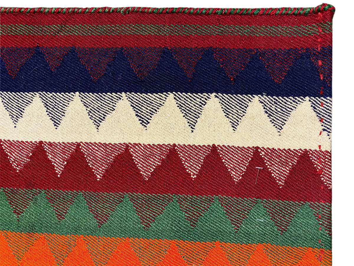 Gros plan d’un tapis Jajim : bandes colorées aux bordures en zigzag et texture tissée