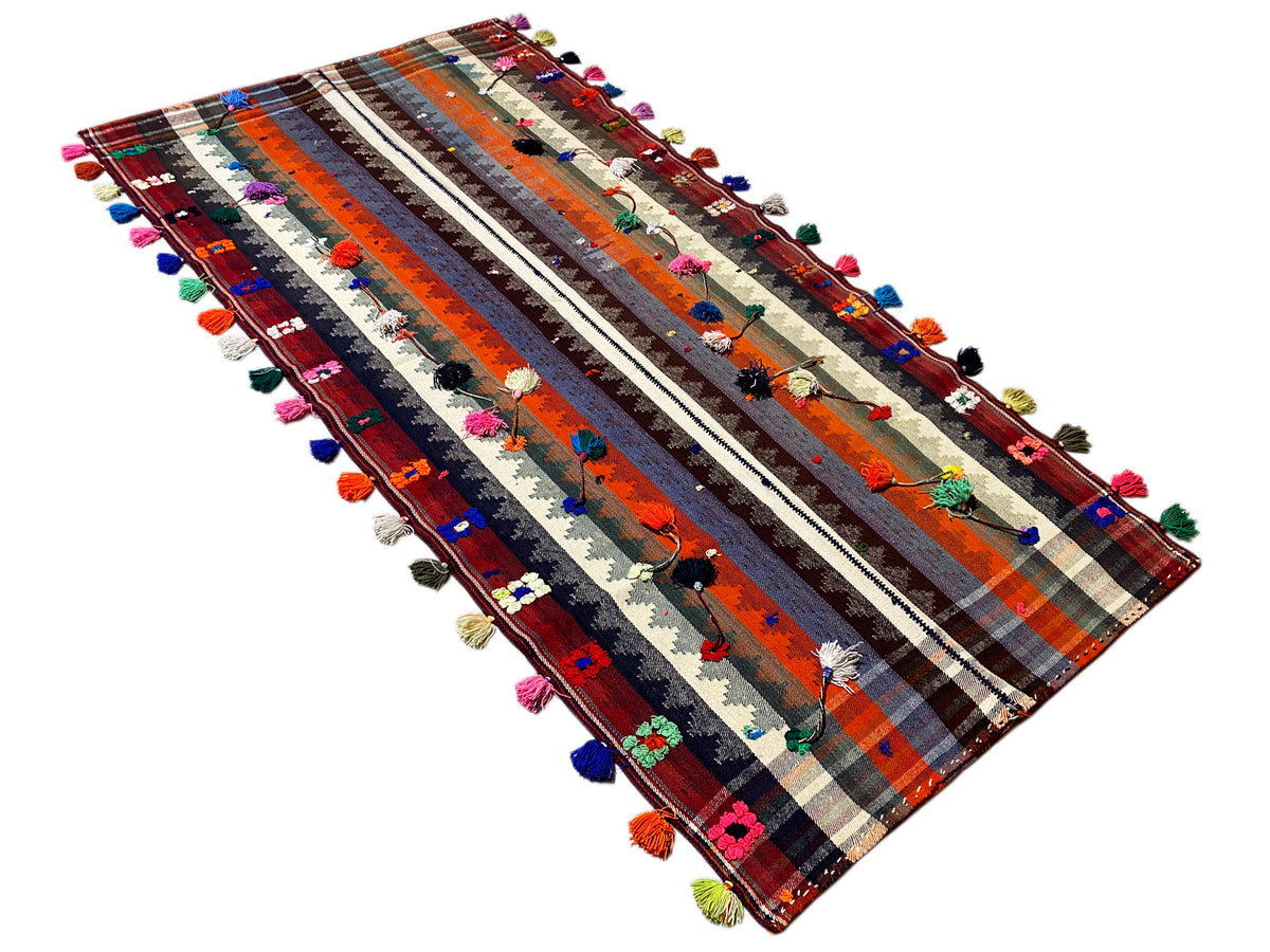 Tapis kilim vu en diagonale, avec des rayures et des pompons colorés sur les bords
