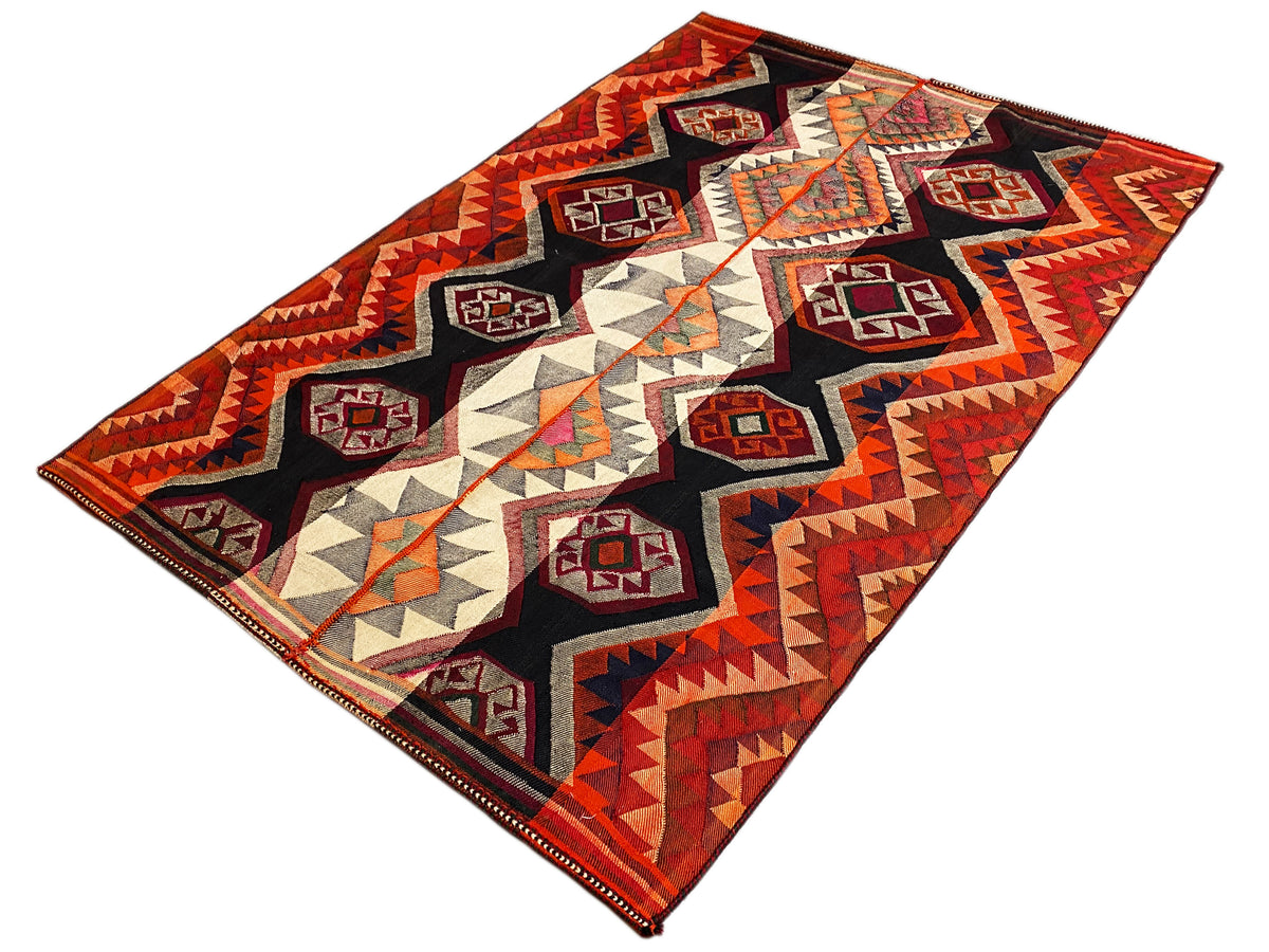 Vue en biais d’un tapis jajim : losanges, zigzags et triangles en rouge, noir et beige
