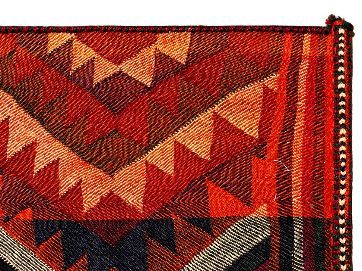 Gros plan d’un tapis jajim : triangles et zigzags en orange, rouge, noir et crème