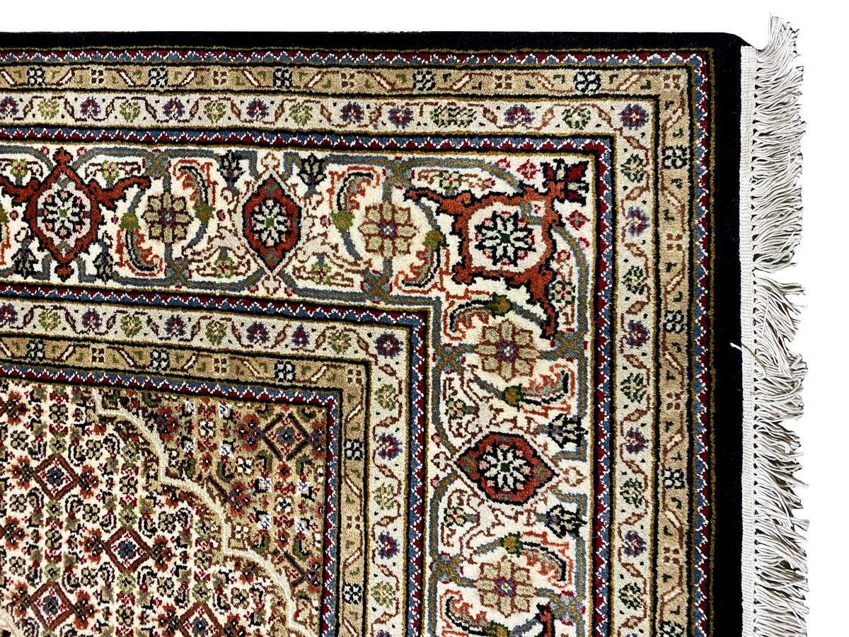 Détail de bordure d’un tapis indo-tabrizien brun avec des ornements colorés et des franges à droite
