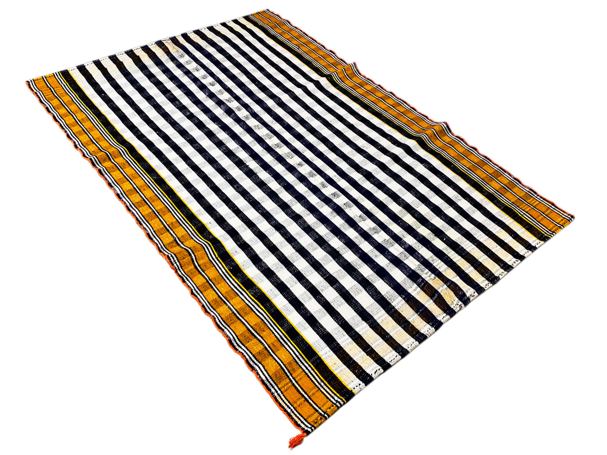 Tapis jajim déployé en diagonale, avec un motif rayé noir et blanc et une bordure orange.