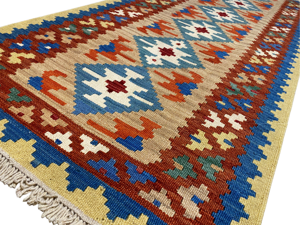 Vue rapprochée d’un tapis kilim : motifs de croix et de losanges en bleu, rouge, vert et crème
