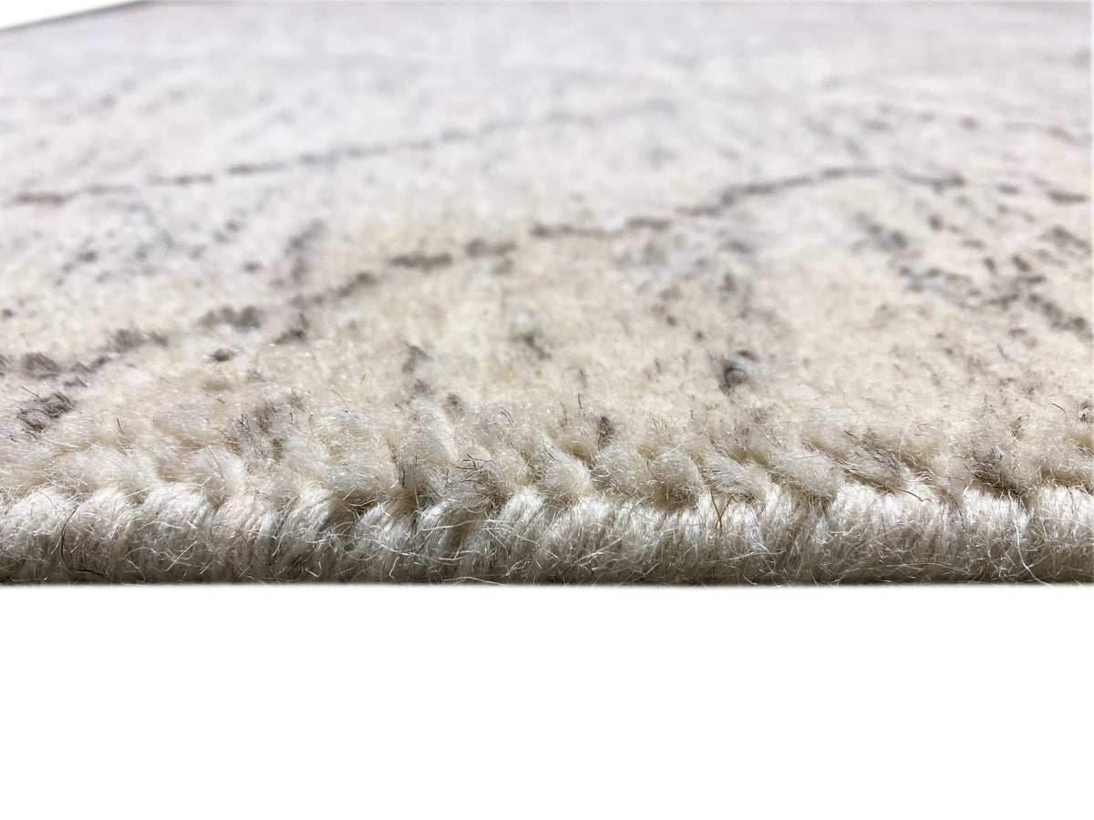 Gros plan sur le bord d’un tapis : fibres denses en beige clair avec un motif gris veiné