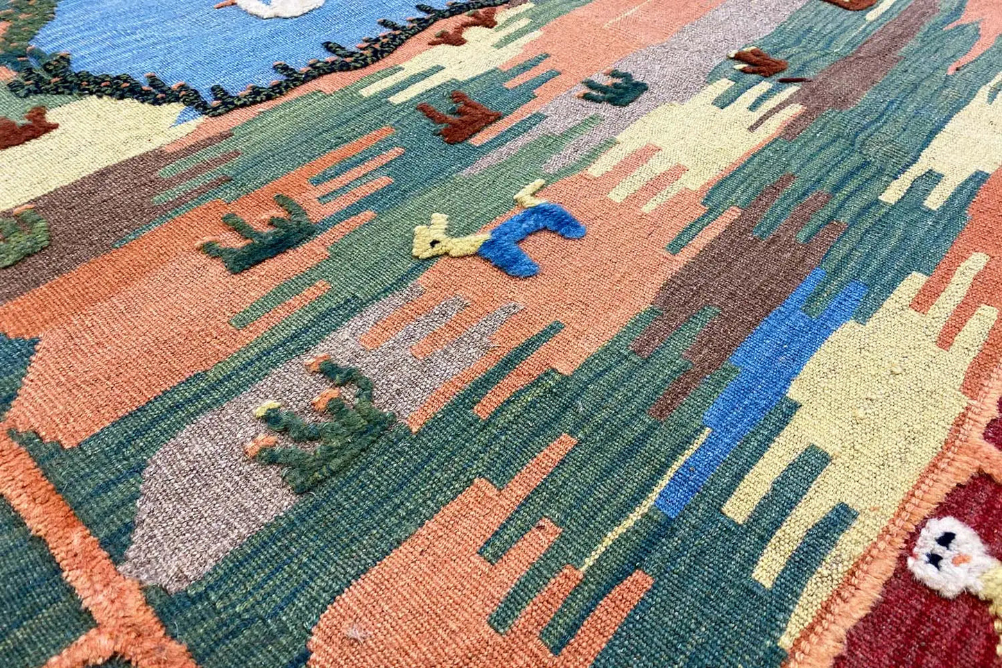Vue rapprochée : kilim aux motifs végétaux et animaliers en bleu, vert, orange et beige
