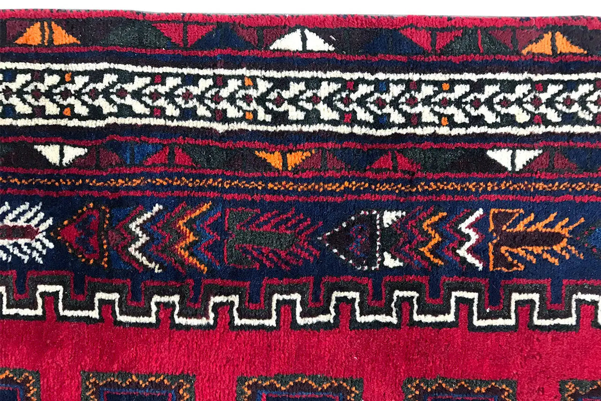 Gros plan : bord de tapis avec des motifs rouges et bleus ainsi que des franges