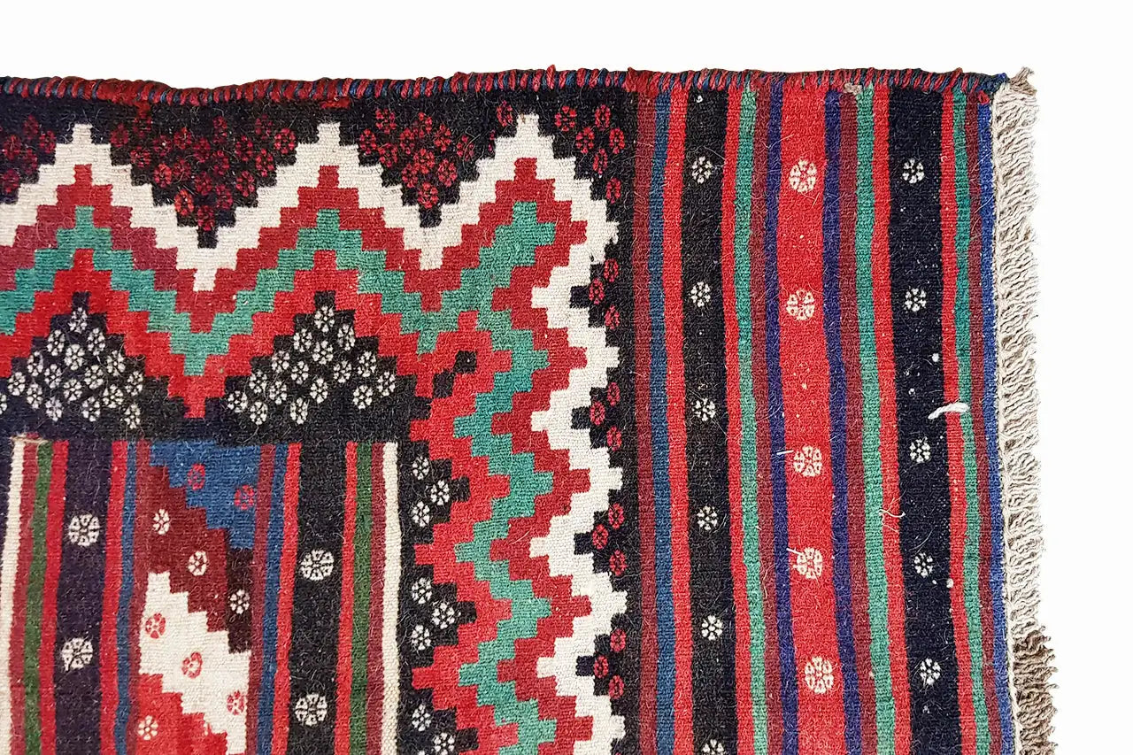 Tapis kilim, bord à franges ; motifs en zigzag et losanges rouges, verts, noirs et blancs.