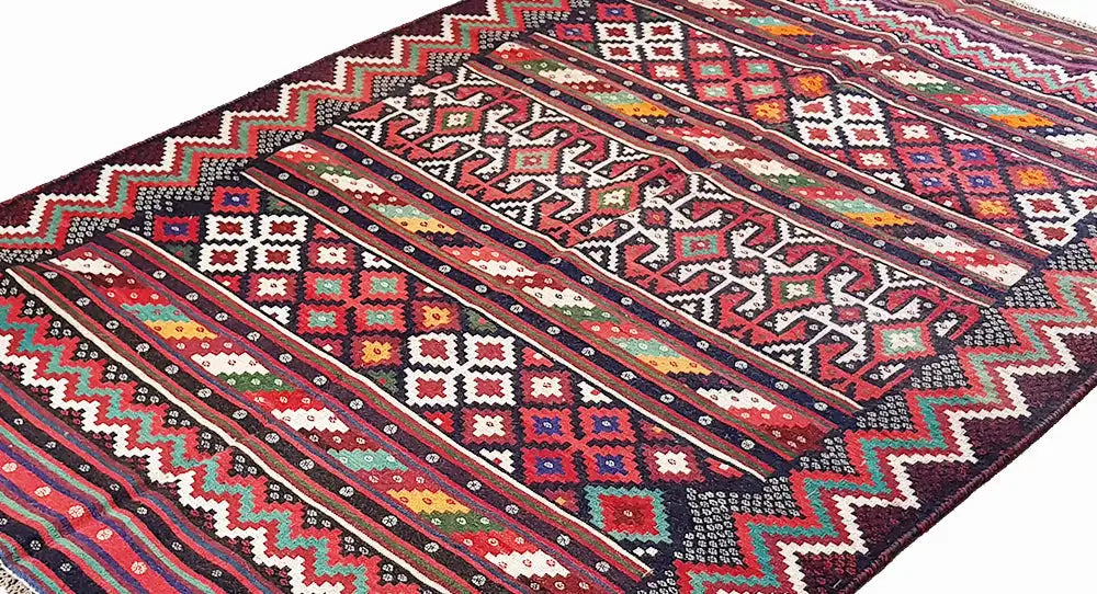 Gros plan d’un tapis kilim : motifs géométriques et rayures en rouge, bleu, vert et noir.