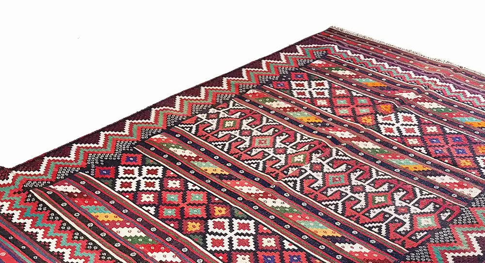 Gros plan d’un tapis kilim : rayures diagonales et motifs en losanges rouges, bleus, blancs et verts.