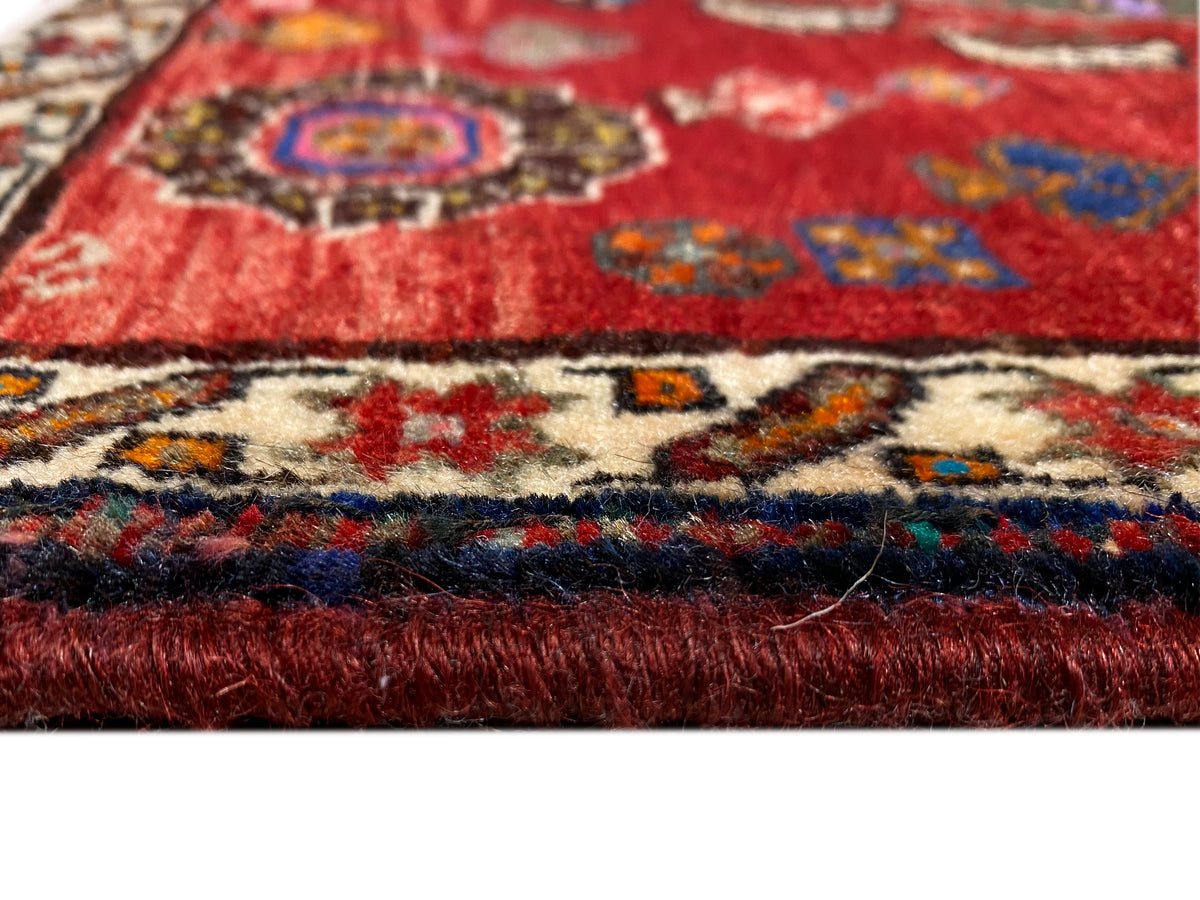 Détail du tapis Poshti 58x57 cm : poil rouge, bordure à motifs colorés et courtes franges
