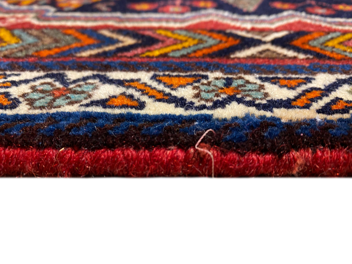 Gros plan du tapis Poshti sur le bord, avec une hauteur de poil dense et une bordure rouge