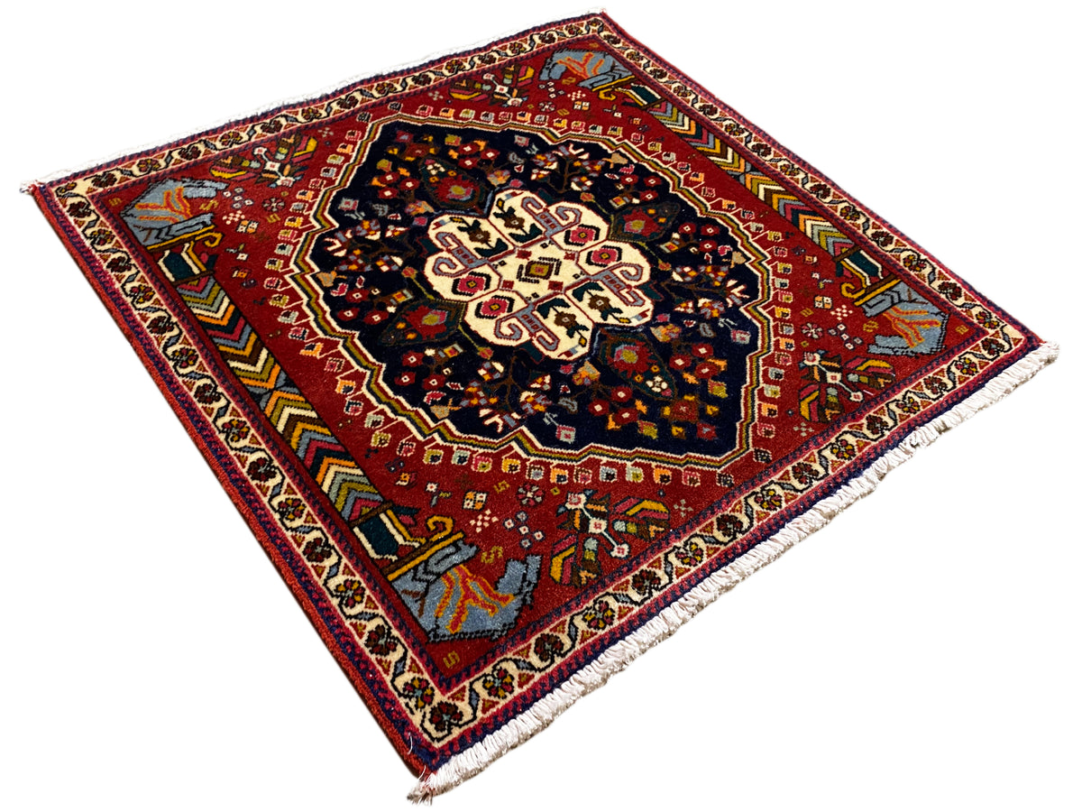 Tapis Poshti à motif rouge multicolore et centre sombre, photographié en biais
