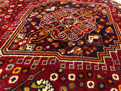 Tapis Poshti 60x60 cm, gros plan de l’ornement central coloré sur fond rouge