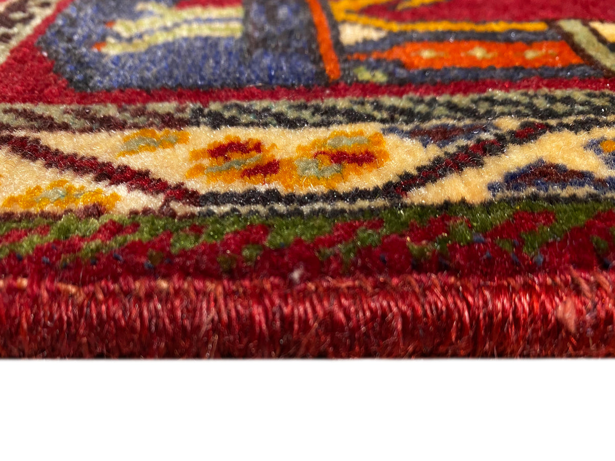 Gros plan du tapis Poshti (59×61 cm) : poils rouges et bordures colorées à franges