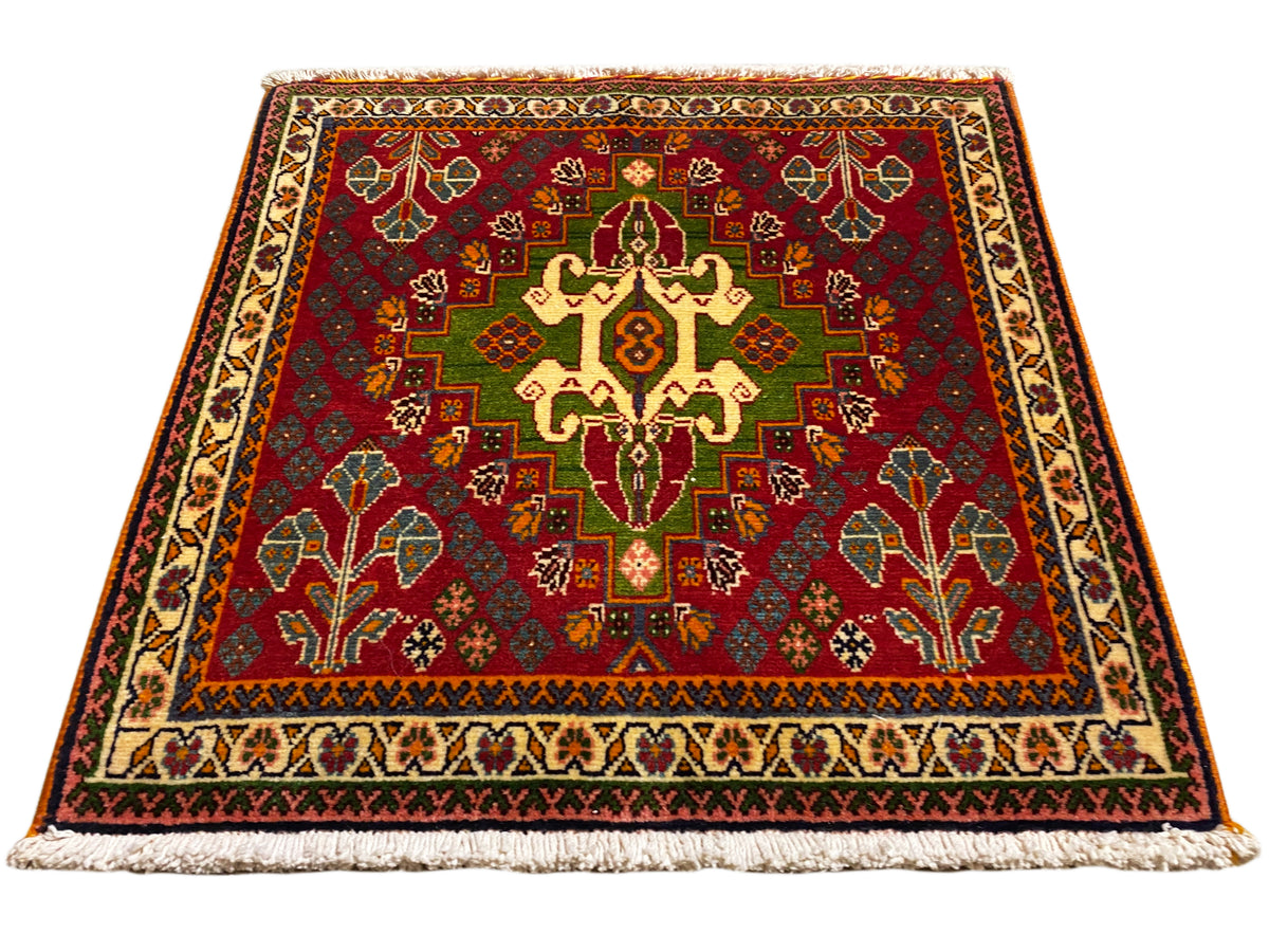 Tapis oriental avec motif central rouge, détails verts et bordure beige, avec franges