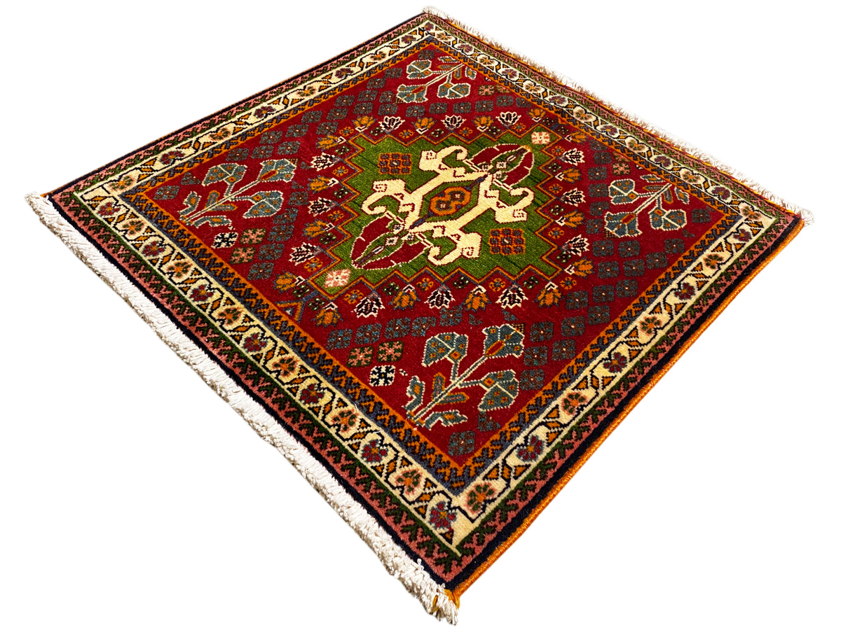 Tapis oriental rouge avec motif central en croix, accents verts et bordure encadrée