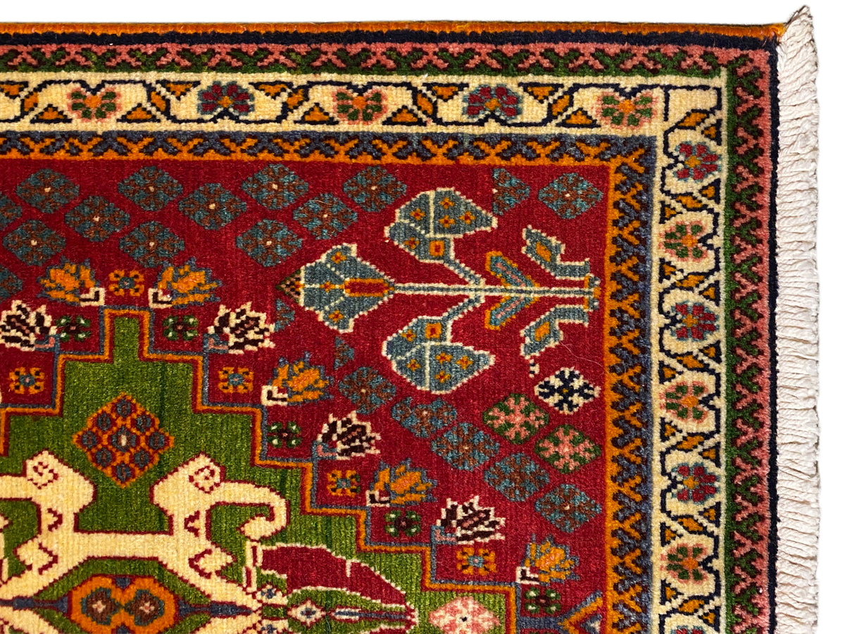 Vue rapprochée : tapis oriental à fond rouge, avec des carrés verts, une bordure à motifs et des franges