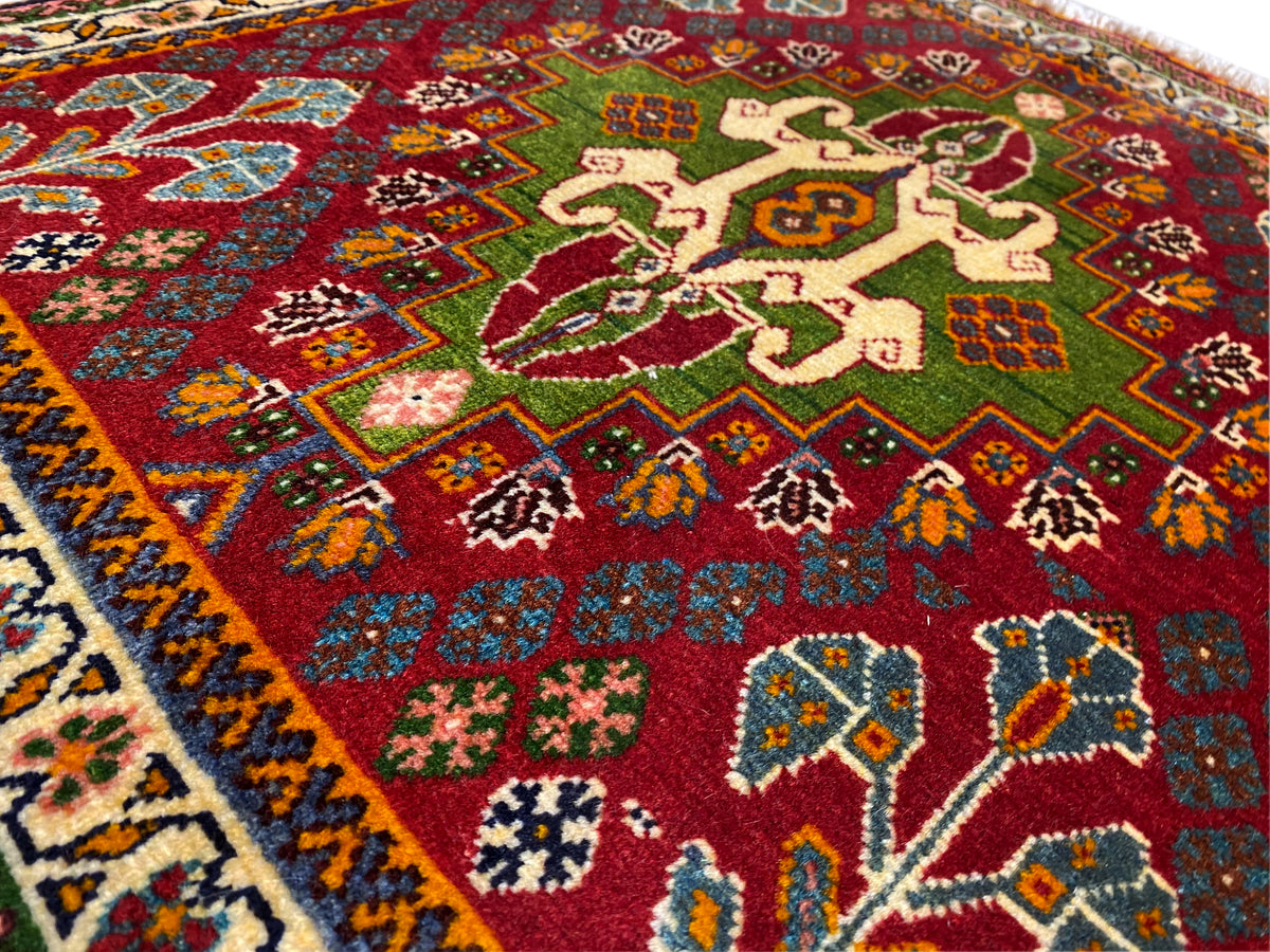Vue rapprochée du tapis oriental : champ rouge aux motifs floraux, avec des touches de vert