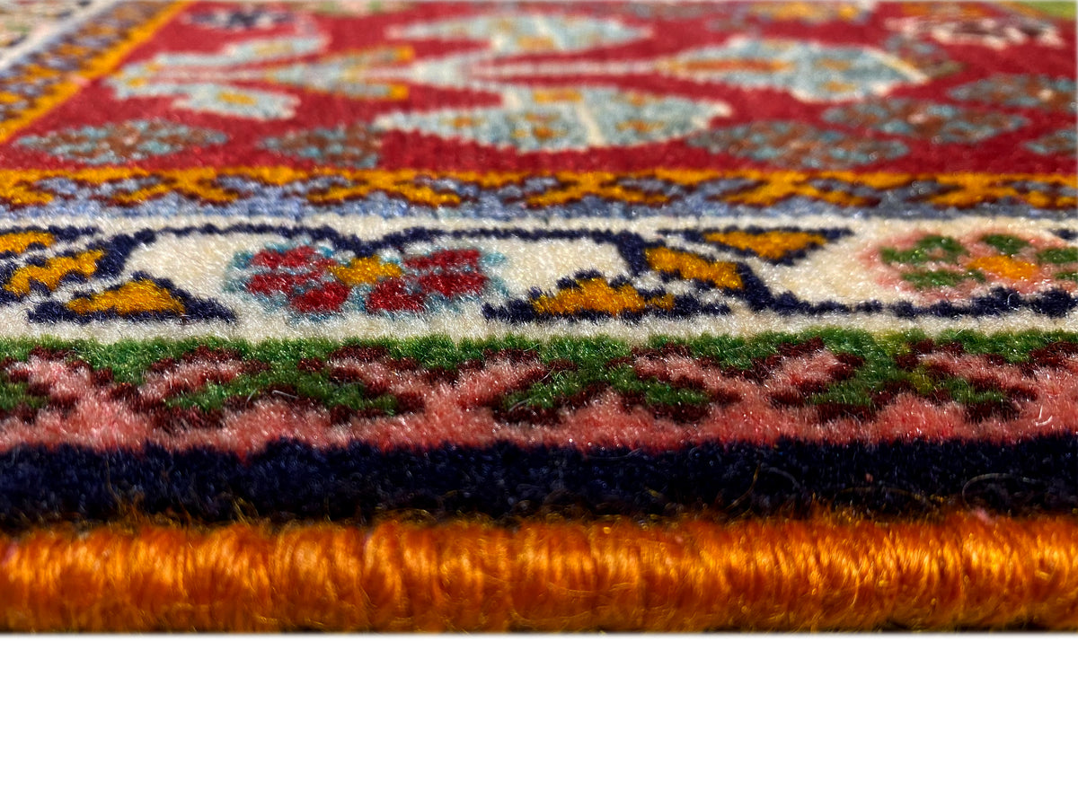 Bord du tapis en détail : poil dense sur fond rouge avec des ornements colorés