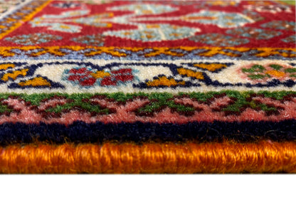 Bord du tapis en détail : poil dense sur fond rouge avec des ornements colorés