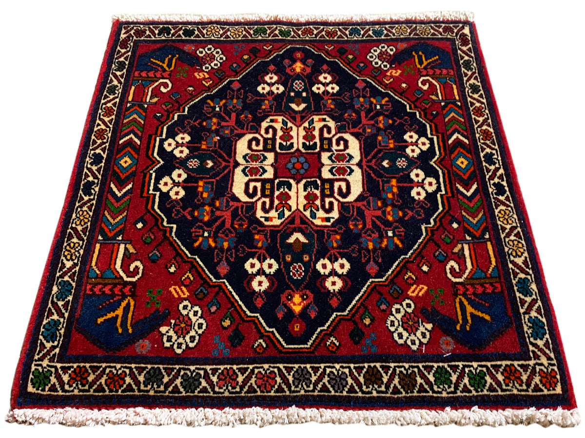 Tapis de forme carrée avec médaillon central, ornements rouges et bleus et franges courtes