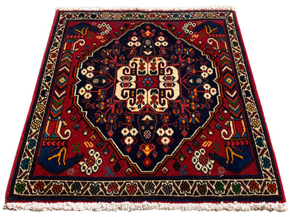 Tapis de forme carrée avec médaillon central, ornements rouges et bleus et franges courtes