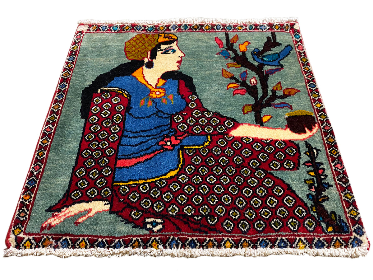 Tapis Poshti 68x63 cm en vue de trois quarts avec personnage, arbre, bordures à motifs rouges, franges