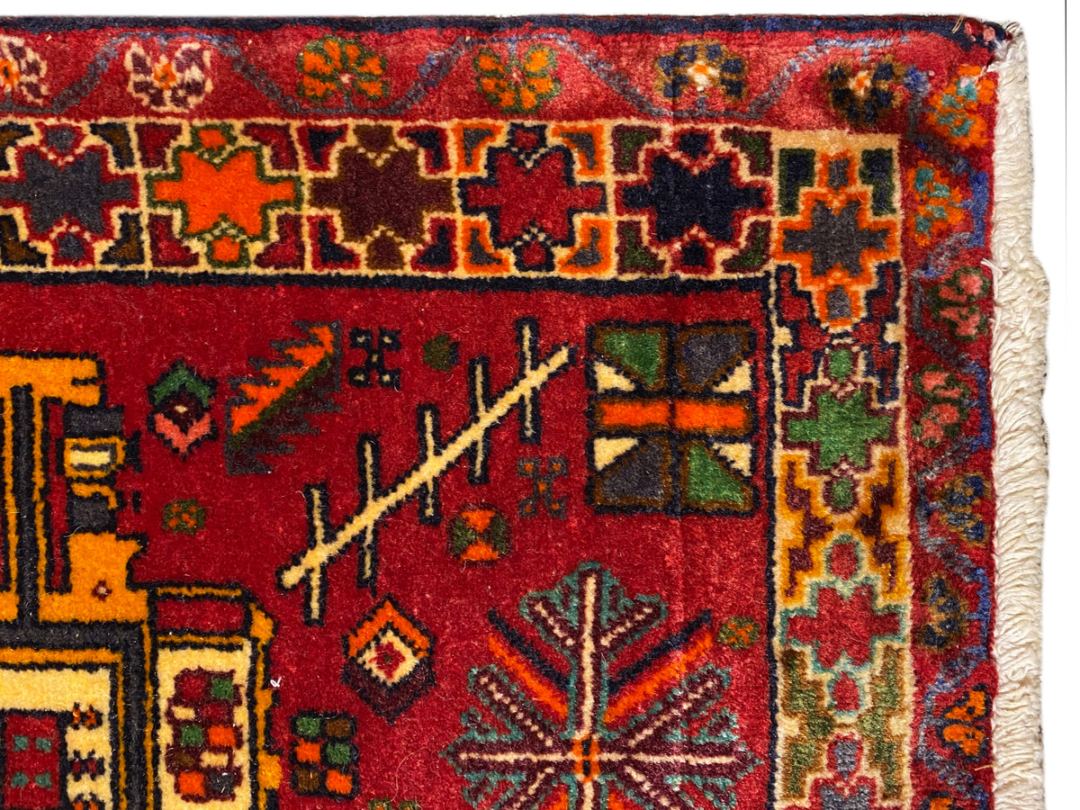 Gros plan : tapis Poshti à fond rouge, orné de motifs colorés et d’une bordure multicolore