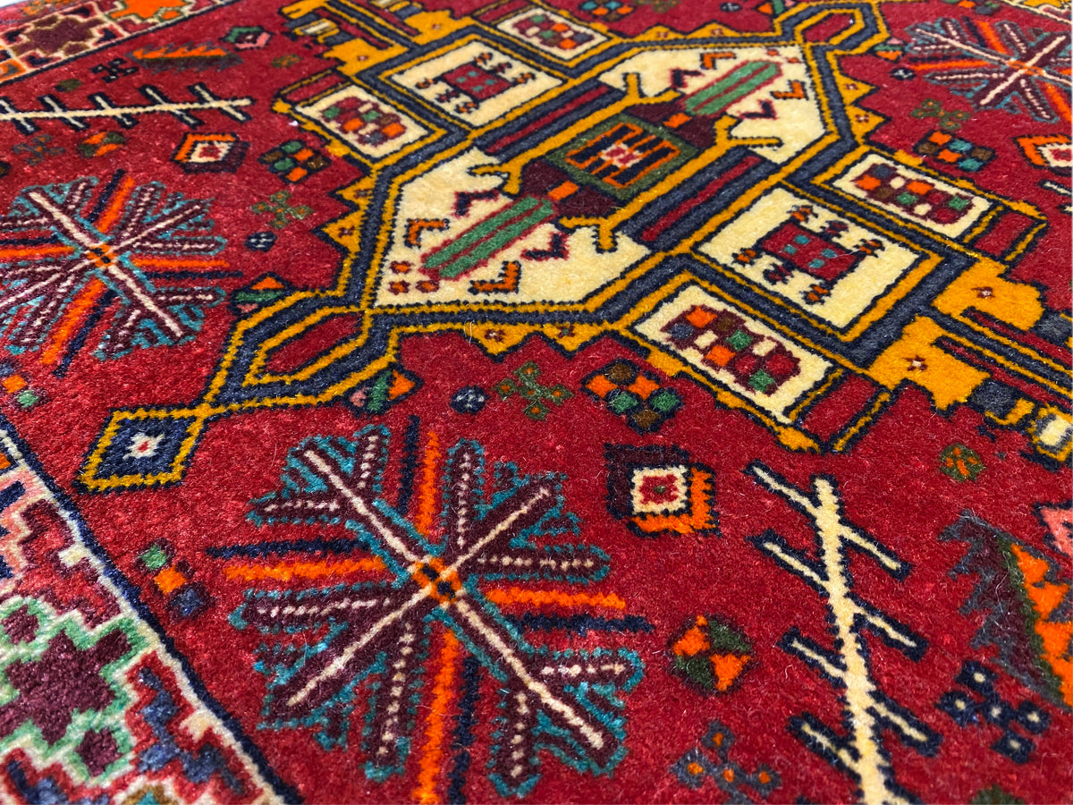 Gros plan : tapis Poshti sur fond rouge avec des motifs géométriques colorés