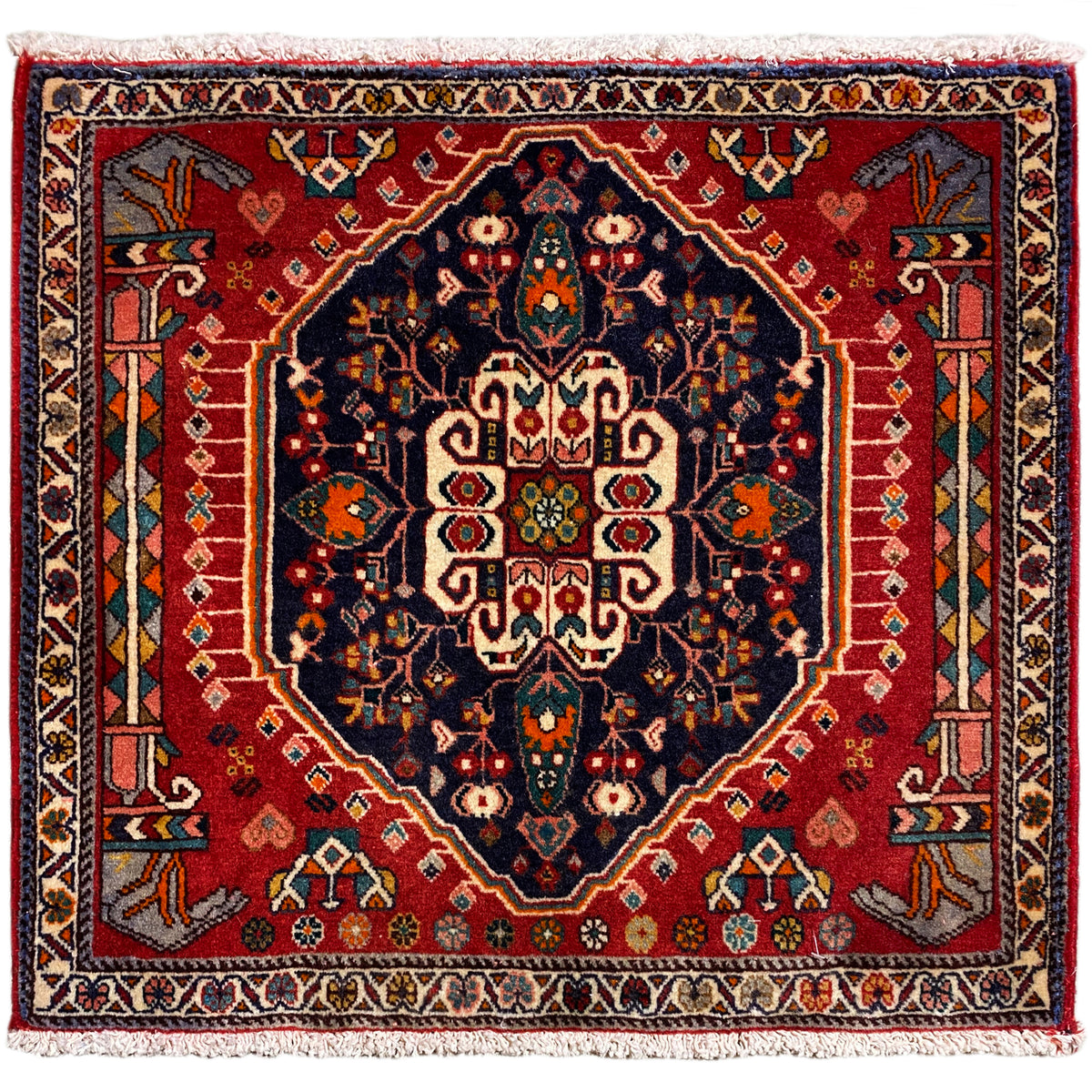 Tapis carré à fond rouge et motif central bleu foncé, avec des franges