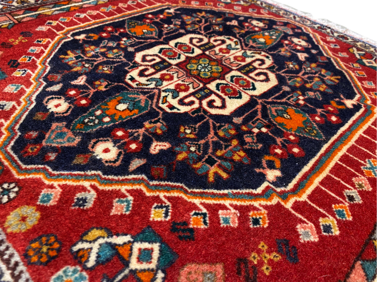 Surface du tapis : motif central sur fond bleu foncé, bordure colorée, franges
