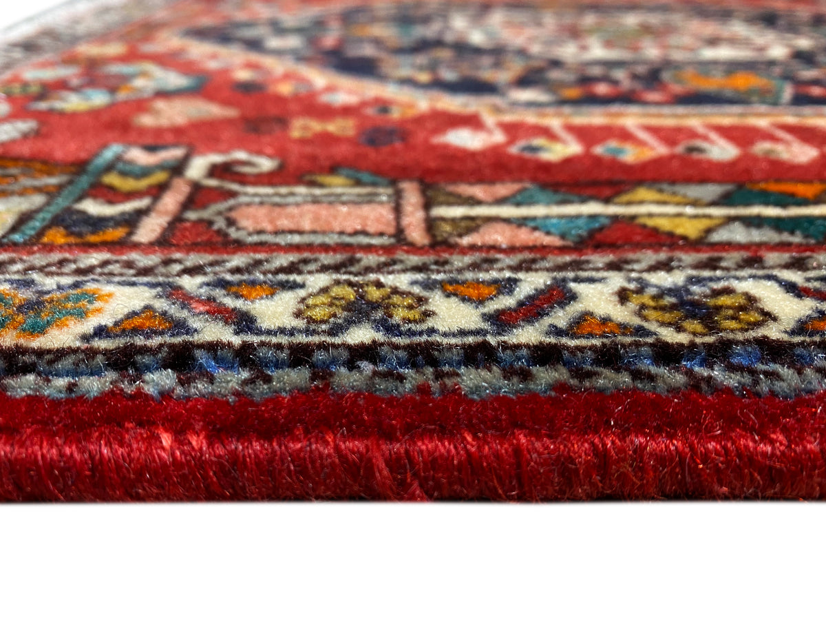 Bordure de tapis en détail : velours rouge, galon à motifs multicolores et franges effilochées