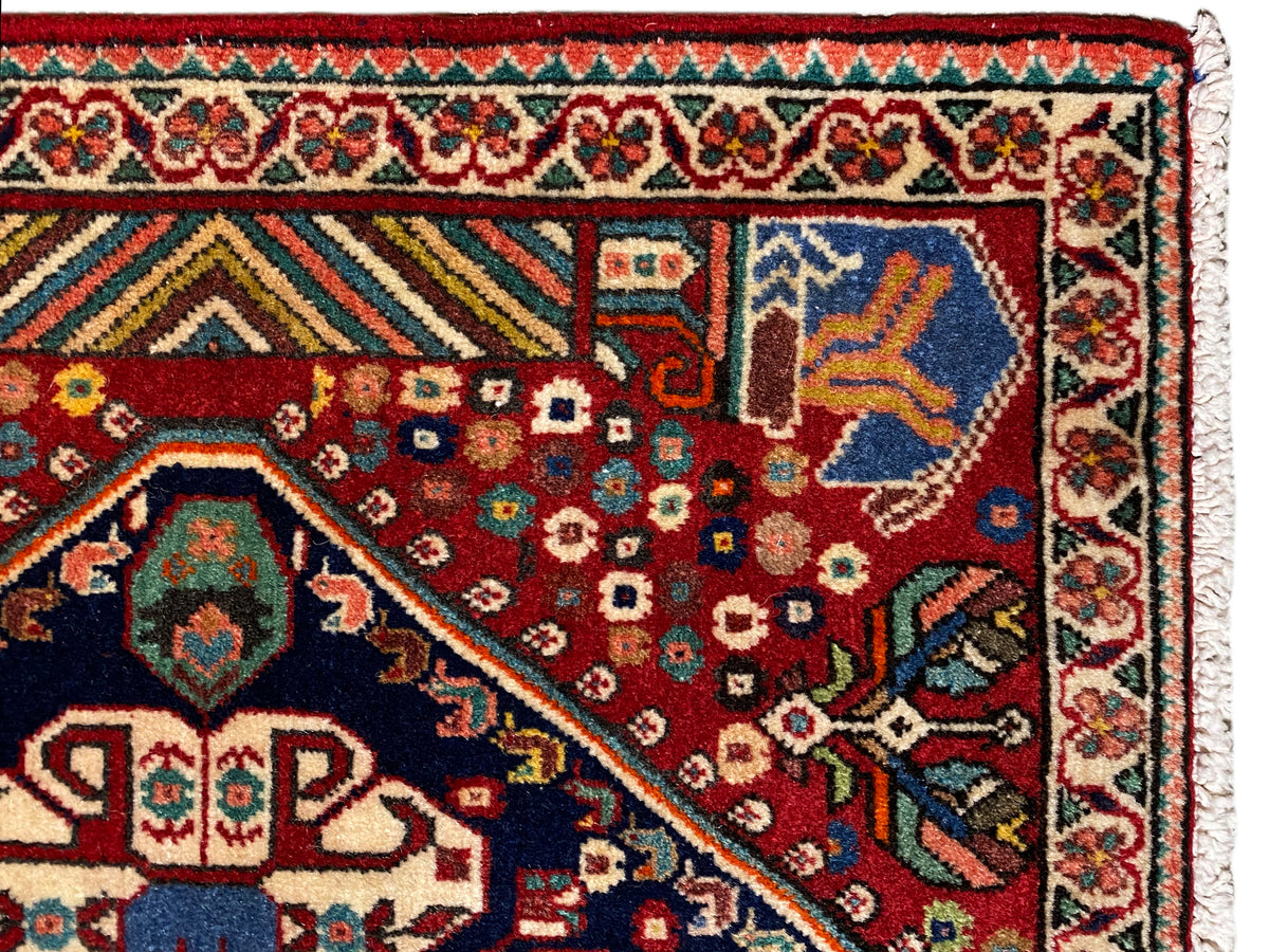 Détail du tapis : champ rouge à motifs géométriques, motif d’angle bleu et bordure