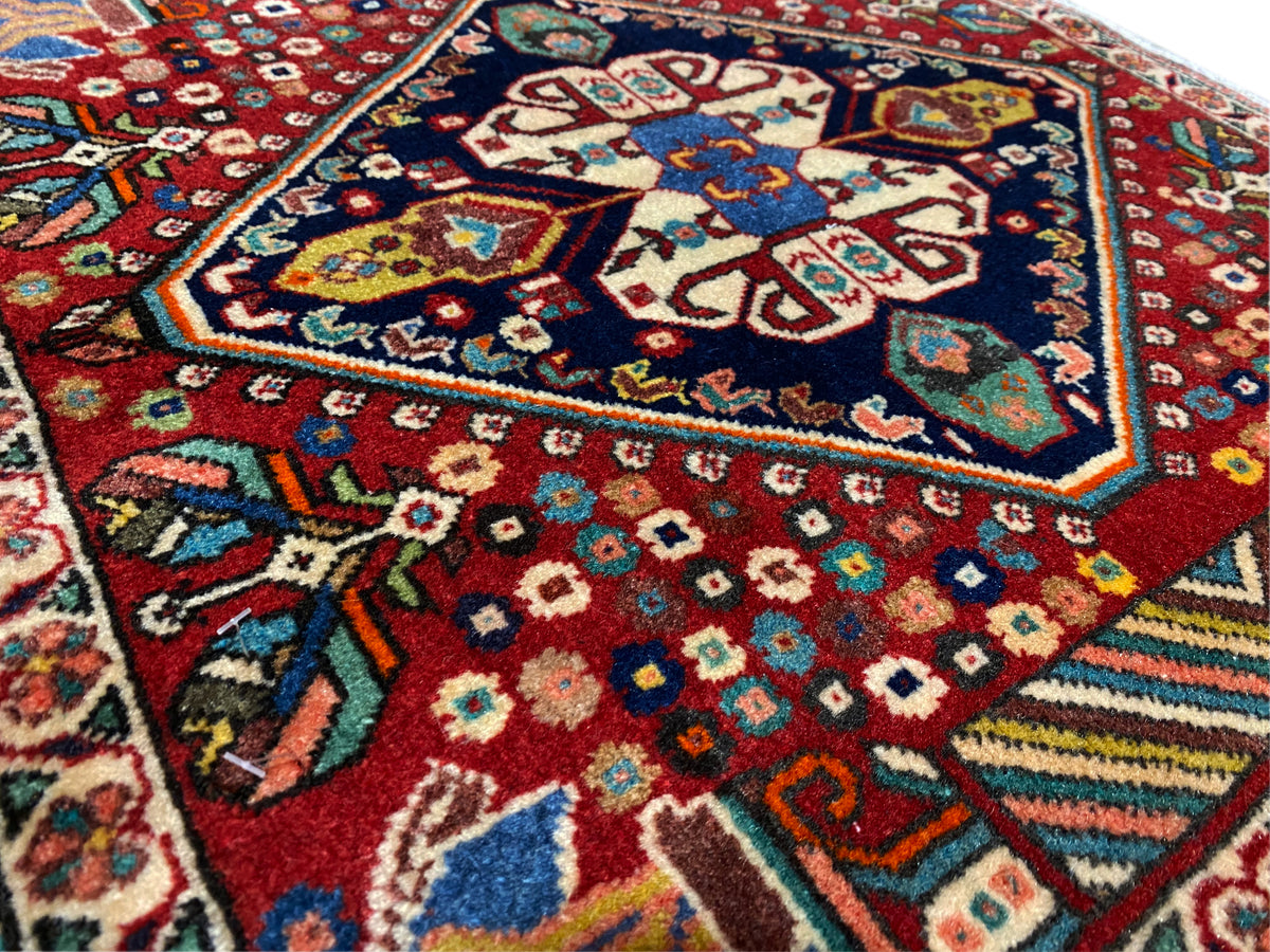 Détail du tapis : losanges colorés et motifs floraux sur fond rouge