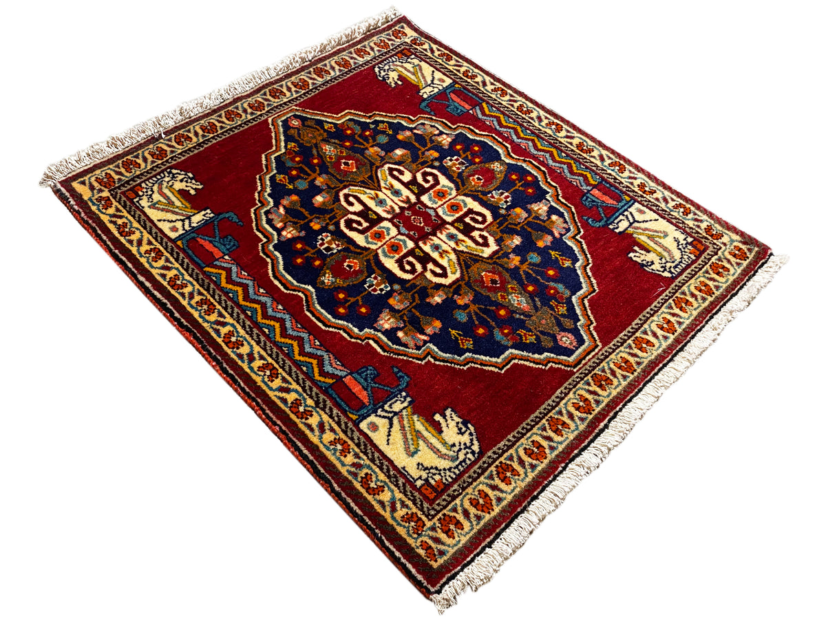 Tapis à motifs losangés sur fond rouge, avec un centre bleu foncé et des franges
