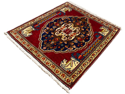 Tapis à fond rouge, motif central bleu foncé, bordures ornementales beiges et franges