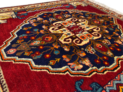 Gros plan sur le centre du tapis : bleu foncé, rouge, beige et motifs ornementaux multicolores