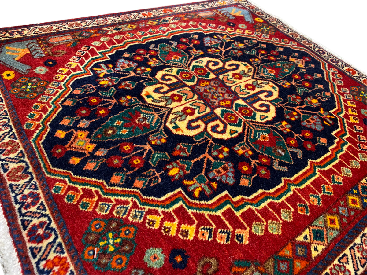 Détail du tapis dans l’angle : motif dense en bleu foncé, rouge, jaune et vert