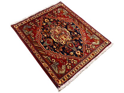Tapis 65x59 cm vu en perspective : bord rouge, motifs sombres, franges latérales