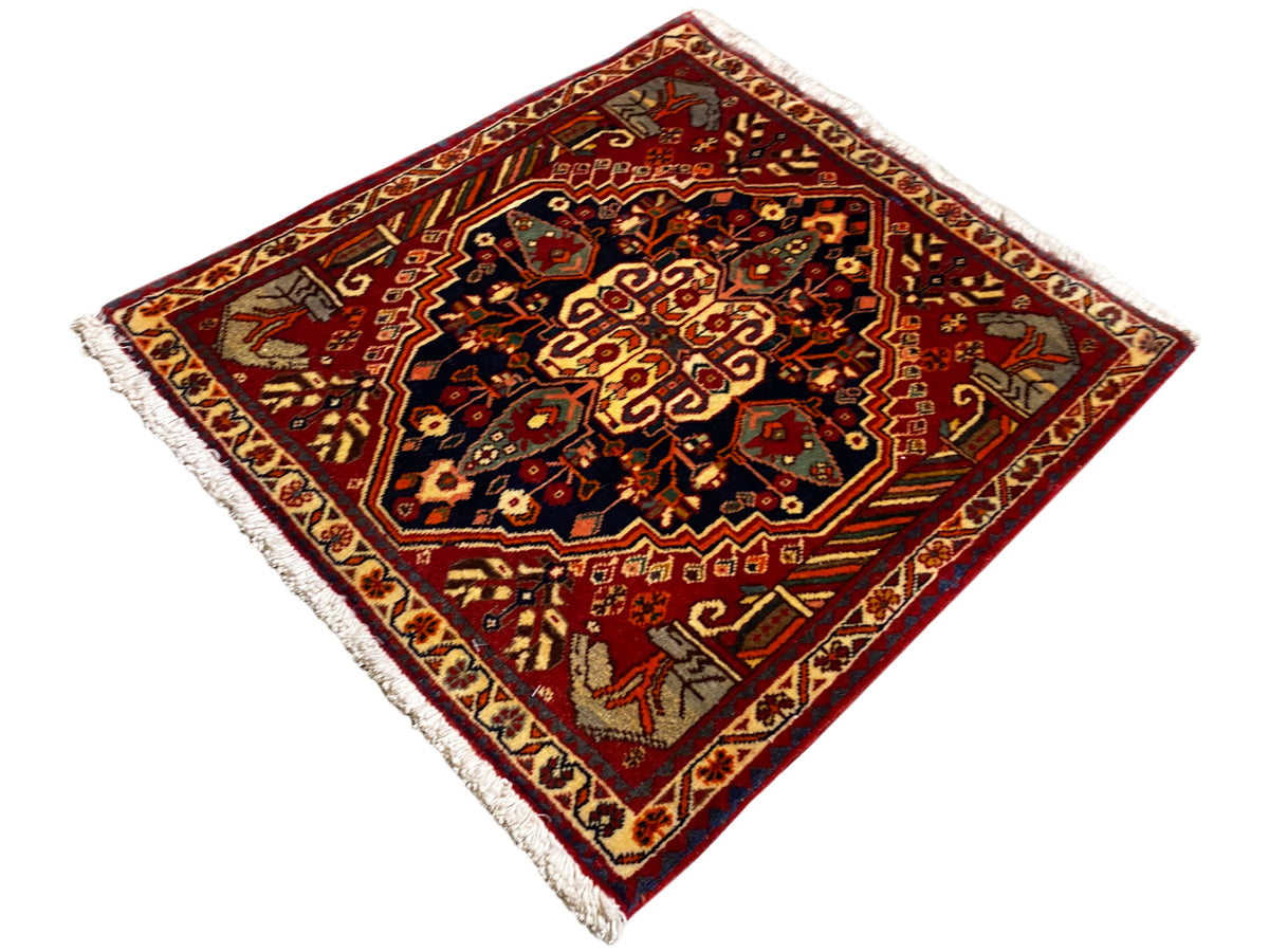 Tapis de 65x59 cm avec fond rouge, ornements centraux foncés et franges sur les bords