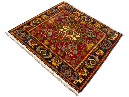 Coin de tapis avec motif rouge, accents verts et bordure sombre, franges
