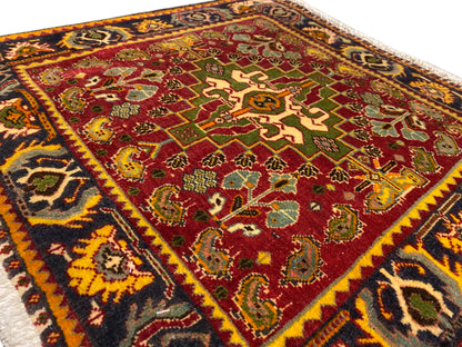 Surface de tapis avec motif central rouge, ornements verts et bordure décorative multicolore