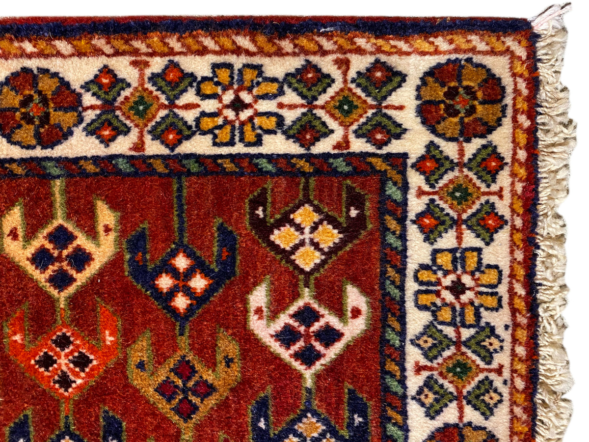 Détail du tapis : surface rouge avec bordure ornementale, losanges colorés et bords latéraux effilochés