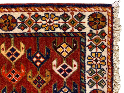 Détail du tapis : surface rouge avec bordure ornementale, losanges colorés et bords latéraux effilochés