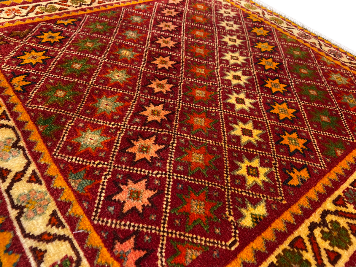Gros plan sur un tapis Poshti : motif d’étoiles et de losanges aux couleurs intenses dans le champ du tapis.